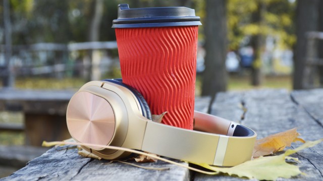 paper cup with a warming drink: tea, coffee or cappuccino and wireless headphones on yellow autumn leaves. relaxation while walking through the autumn park. beauty in nature
